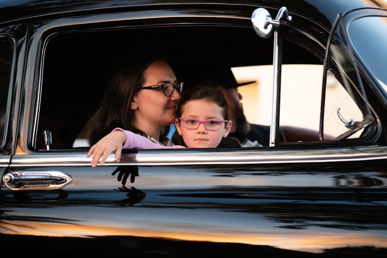 A mother and daughter enjoy a car ride in a vintage black automobile, capturing a serene family moment.