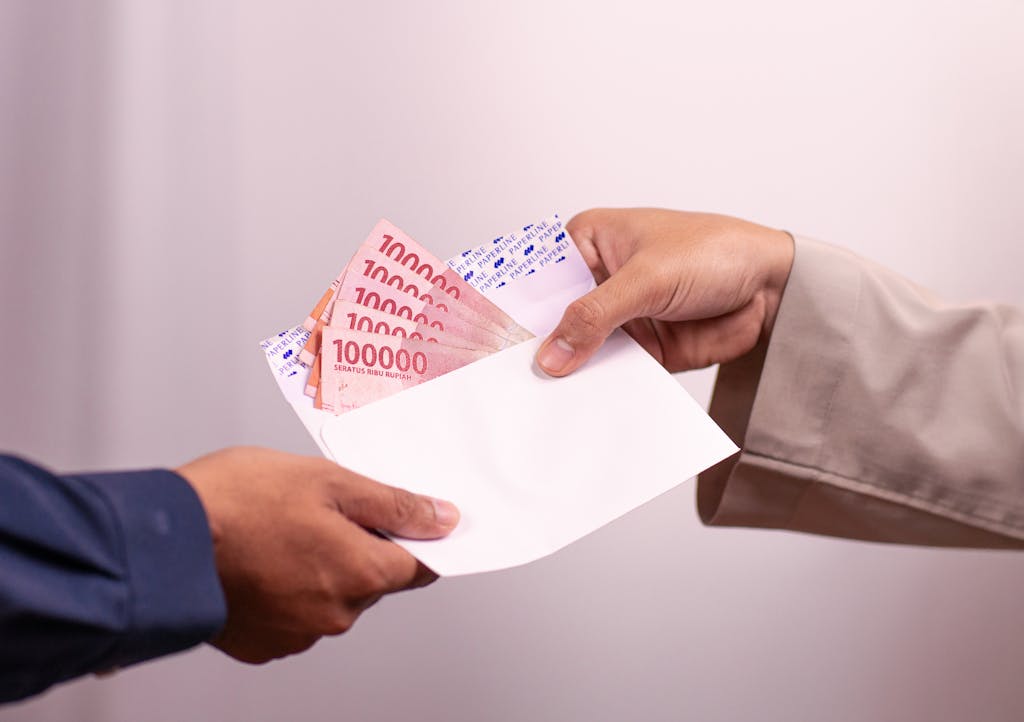 Hands giving and receiving Indonesian rupiah in an envelope, symbolizing financial transaction.