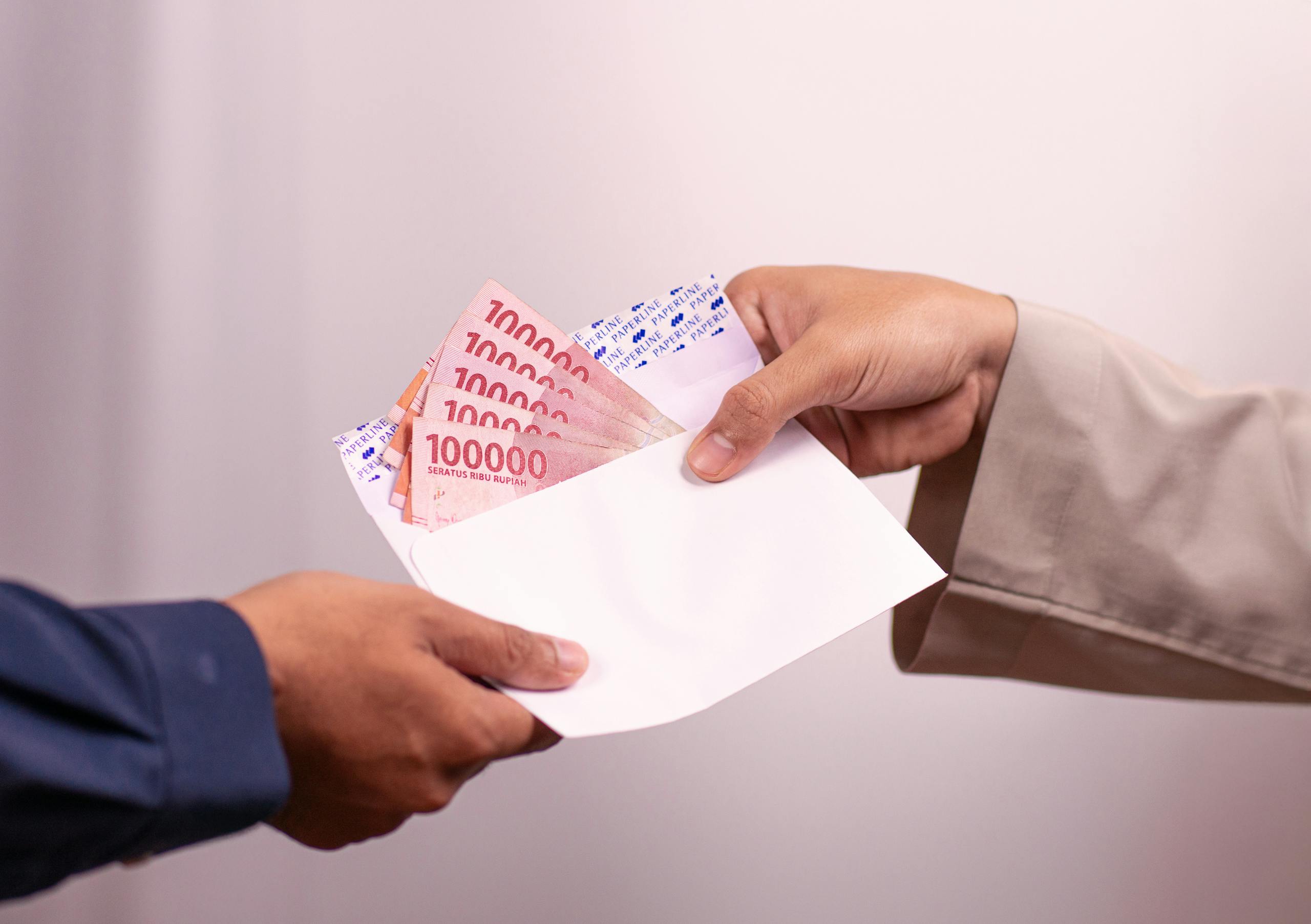 Hands giving and receiving Indonesian rupiah in an envelope, symbolizing financial transaction.
