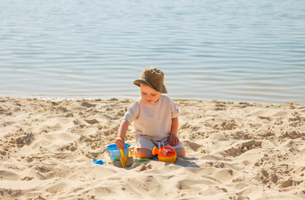 A young boy enjoying a sunny day at the beach, playing with toys in the sand.