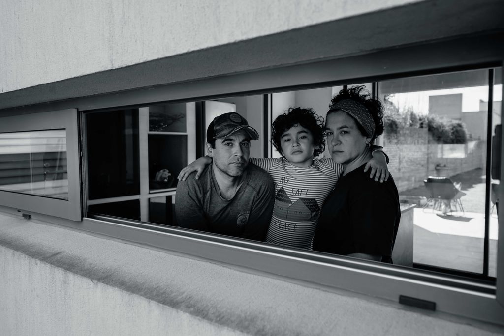A black and white portrait of a family trio gazing out from a window frame, capturing a reflective moment.